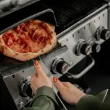 Pizza na grillu, jak piec bez kamienia. Ręka z paznokciem w kształcie pizzy zbliża się do gorącego dania.