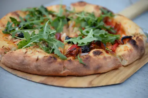 Pizza z rukolą, oliwkami i papryką na twardym cieście do pizzy, podana na drewnianej desce.